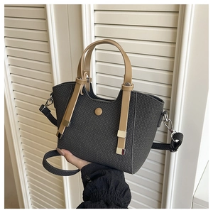 Detail of grey bucket bag with brown handles, woven texture and gold hardware