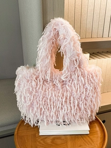 Sac fourre-tout rose en plumes pelucheuses posé sur une table dans un décor chaleureux