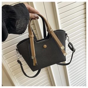 Detail of black woven basket bag with brown leather handles and adjustable shoulder strap