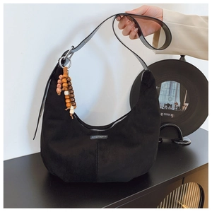 Detail of black suede hobo bag with ethnic beaded tassel and minimalist logo label
