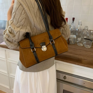 Brown suede shoulder bag with black leather straps shown in a warm kitchen setting