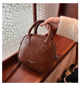 Close-up of brown leather handbag featuring stitching details and round handles on wood