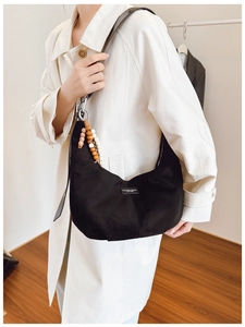 Detail of black suede hobo bag with wooden bead charm and fashion leather label
