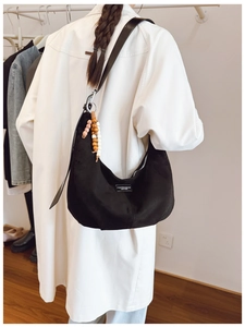 Detail of black suede hobo bag with a beaded charm and fashion label worn with a coat