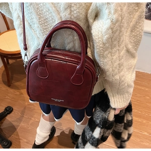 Detail view of wine red leather handbag with stitching, dual handles and thin shoulder strap