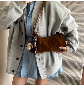 Detail of a dark brown suede crescent shoulder bag featuring a cute plush puppy pendant