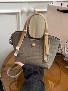 Brown woven bucket bag with khaki leather straps shown on a stylish glass table