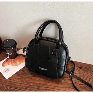 Detail of black quilted leather crossbody bag with top handles on a wooden table