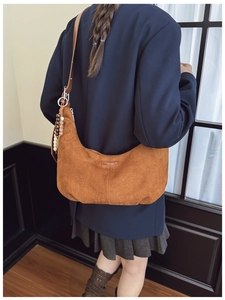 Close-up of brown suede hobo bag with wooden bead charm and leather shoulder strap