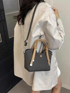 Chic dark grey woven bucket bag with brown leather strap worn crossbody by a model