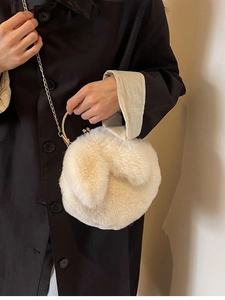 Schicke cremeweiße Kunstfell-Beuteltasche mit Hasenohren und Goldkette auf schwarzem Mantel