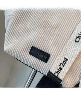 Detail of off-white corduroy texture with leather logo tag and printed cotton strap