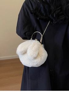Plüschige cremeweiße Hasenohr-Eimertasche mit goldenen Metallgriffen und Kette auf Mantel