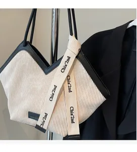 Detail of cream corduroy tote bag with black leather trim and chic lettered ribbon
