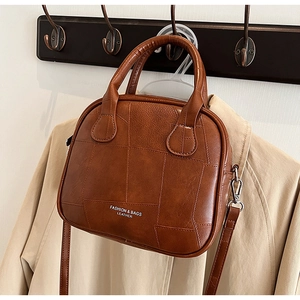 Detail view of a brown vintage patchwork handbag hanging on a trench coat stylishly