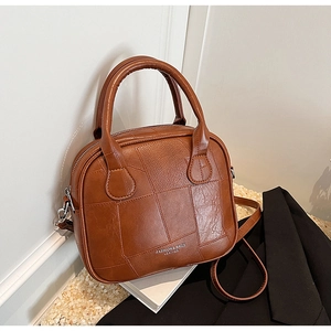 Detail of a brown tote bag featuring irregular patchwork texture and silver hardware accents