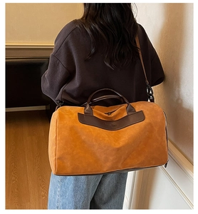 Detail of a ginger yellow travel bag with brown leather handles worn by a model