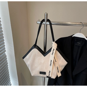 Detail view of beige corduroy tote bag featuring black leather trim and stylish logo ribbon