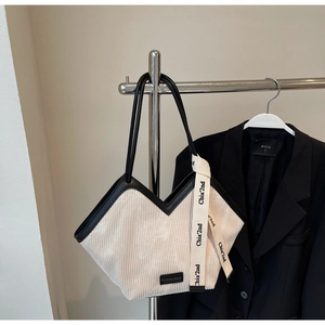Detail view of corduroy tote bag with black leather trim and decorative fashion ribbon
