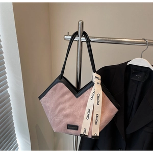 Detail of pink corduroy tote bag featuring black leather trim and decorative ribbon