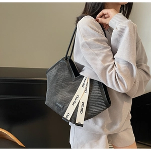 Detail of grey corduroy tote bag with black trim and decorative logo strap on shoulder