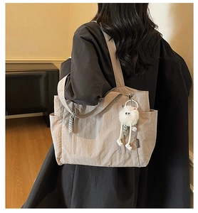 Detail view of khaki nylon tote bag with side pockets and a cute plush monster charm