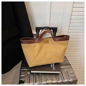 Detailed shot of yellow quilted tote bag with brown handles on a grey suitcase