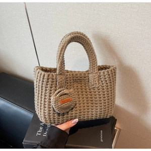 Detail of hand woven knit tote bag with handmade leather tag on neutral background