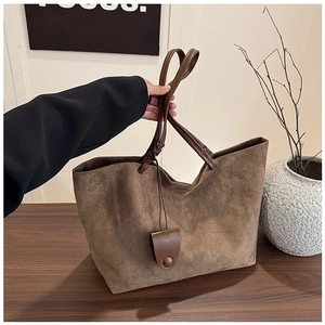 Detail of dark brown faux suede tote bag with long handles and decorative pendant