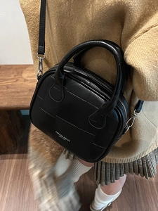 Chic black quilted semi-circle leather handbag worn with casual knitwear
