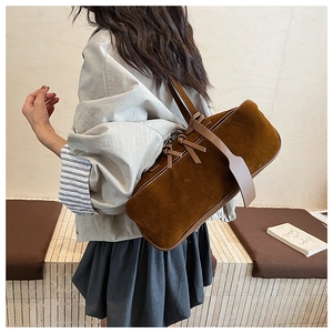 Detail view of brown suede pillow bag with bow tie accent on model's shoulder