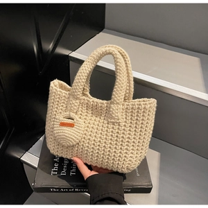 Detailed close-up of beige handmade knit tote bag with 'Hand Made' leather charm tag