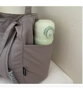 Detail of grey nylon tote side pocket holding a water bottle with woven zipper pull