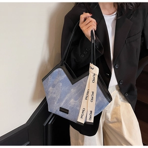 Detail of blue corduroy tote bag with black leather piping and stylish lettered ribbon