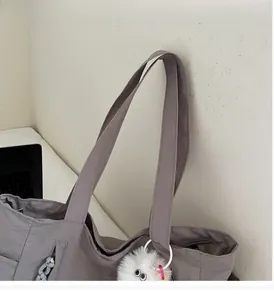 Detail of durable nylon tote bag featuring side pockets and a cute plush ball charm
