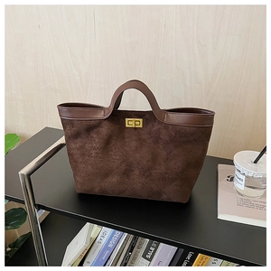 Detail of dark brown suede tote featuring quilted stitching and a golden turn-lock