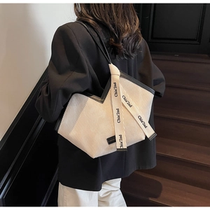 Detail of pleated cream tote bag with black leather straps and decorative logo ribbon