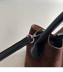 Detail of silver metal hardware on dark brown suede bucket bag with black leather strap