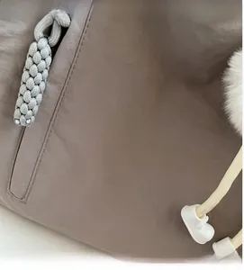 Close-up of taupe nylon tote bag featuring a grey woven zipper and a white faux fur charm
