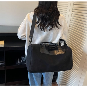 Rear view of a model carrying a large black duffel bag with leather handles and nylon strap