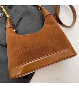 Détail du sac à main en daim marron avec logo embossé et boucle métallique sur blazer gris