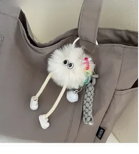 Detail of white monster plush keychain with long legs and large eyes on a nylon tote bag