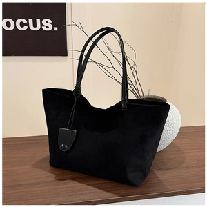 Minimalist black matte leather tote bag shown on a wooden desk with a shield charm detail