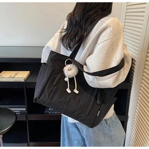 Detail of black nylon tote bag featuring side pocket and cute white doll pendant