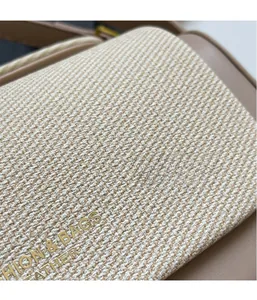 Dettaglio di tela tessuta beige e pelle kaki con logo dorato in rilievo sulla borsa