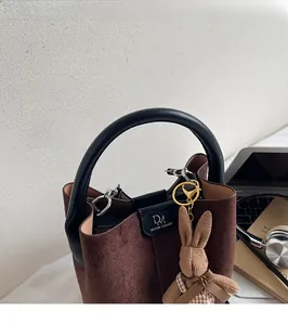 Detail of a brown suede bucket bag with black handles and a cute rabbit charm