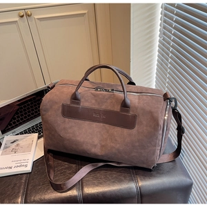 Detail of a large brown suede travel bag with dual handles and embossed leather patch