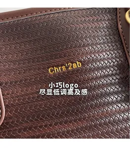 Detail of dark brown woven leather texture with a gold embossed logo on a shoulder bag