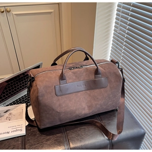 Brown suede travel bag with brand leather patch and dual handles on a leather stool