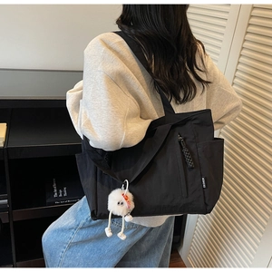 Close-up of a large black nylon tote bag featuring a cute white plush ball keychain
